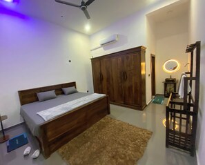 Un dormitorio con cama, armario, tocador con espejo, ventilador de techo y unidad de aire acondicionado.