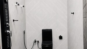 Un baño moderno con inodoro negro, ducha con panel de control y ventilador.