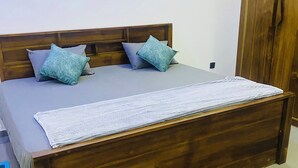 Una cama con cabecera de madera, ropa de cama gris y dos almohadas.