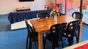 Un comedor con una mesa de madera, sillas negras, camino de mesa rojo y un televisor montado en la pared.