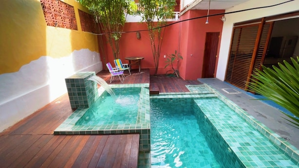 Una piscina con cascada, terraza de madera y una pequeña mesa con sillas.