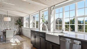 Et moderne køkken med store vinduer, et spiseområde og et træloft.