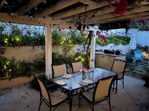 Eine Terrasse im Freien mit Esstisch, umringt von Stühlen, mit Lichterketten und Pflanzen dekoriert.