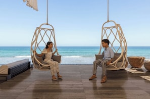 Zwei Personen sitzen auf Korbschwingstühlen mit Blick auf das Meer.