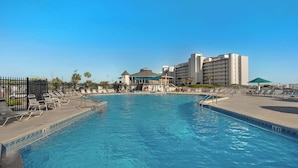 Ein Swimmingpool mit Liegestühlen, einem Zaun und einem Hotelgebäude im Hintergrund.