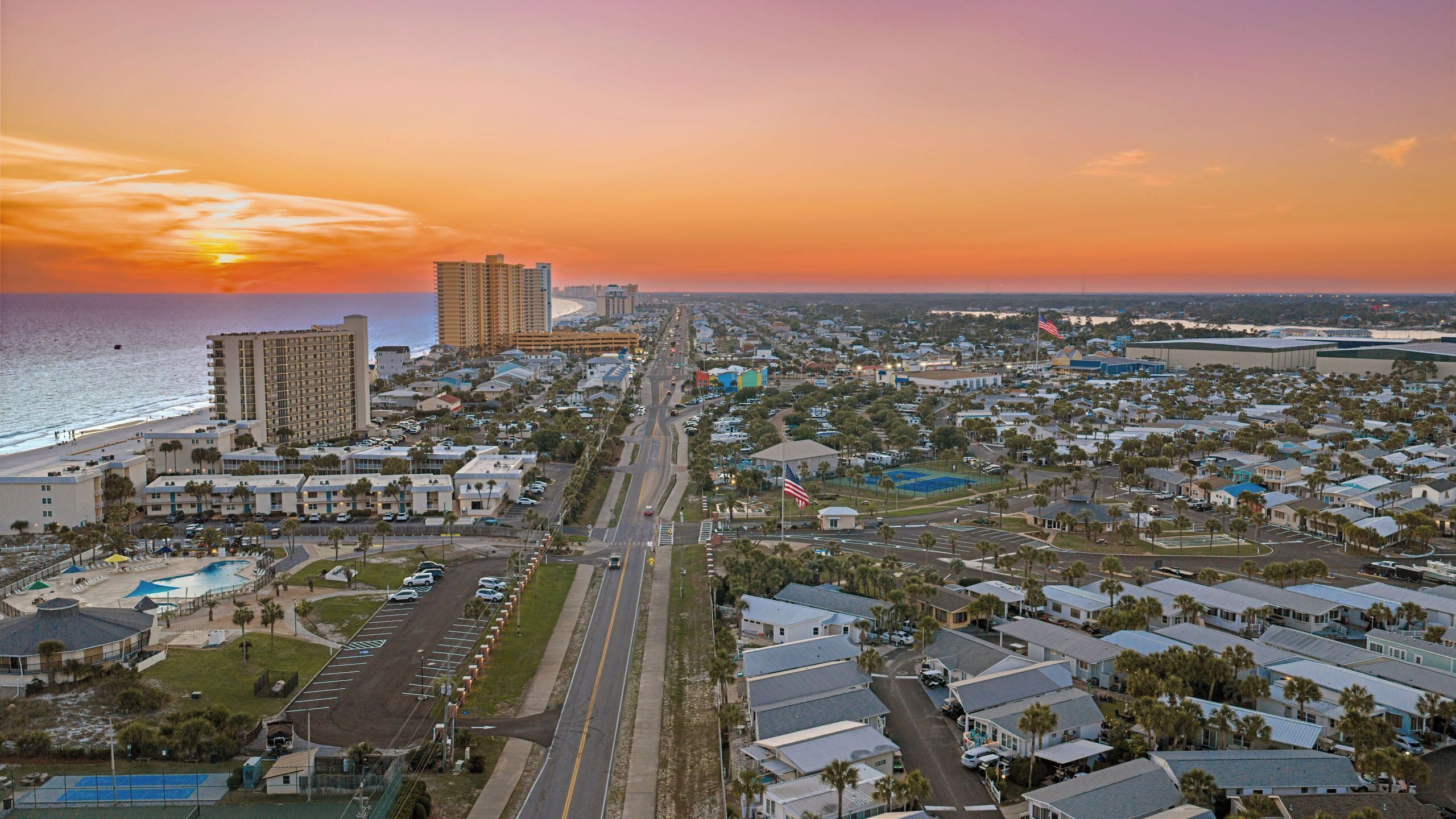 Un paysage urbain côtier avec un hôtel imposant, une plage et un ciel dégagé au coucher du soleil.