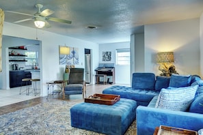 A living room with a blue sofa, ottoman, and a dining area with a piano. - Dog-Friendly home with quick access to the beach and downtown with heated pool. (Stuart)