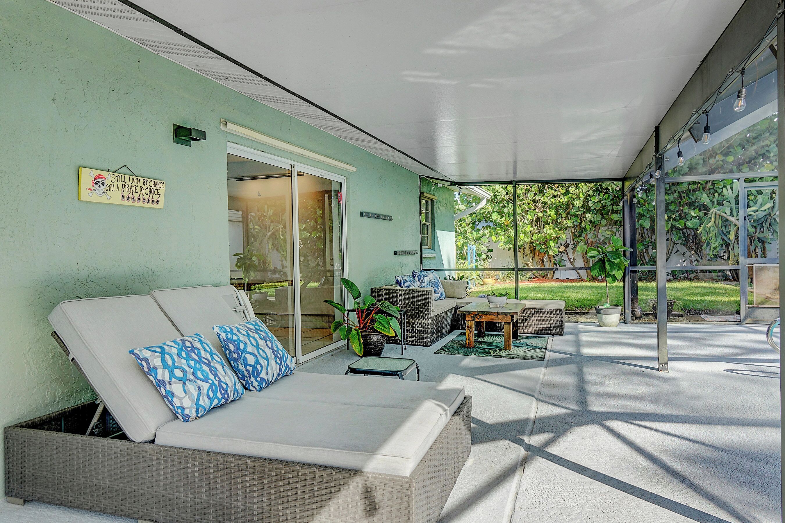 A covered outdoor seating area with a wicker sofa, a potted plant, and a glass door leading to a patio.