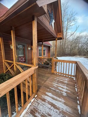 Una cabaña de madera con un porche, una ventana en forma de corazón y una terraza cubierta de nieve.