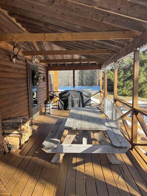 A wooden deck with a covered seating area, a grill, and a view of a snowy landscape. - Log Cabin - Hot Tub - Near Kalahari & Camelback (Newfoundland)