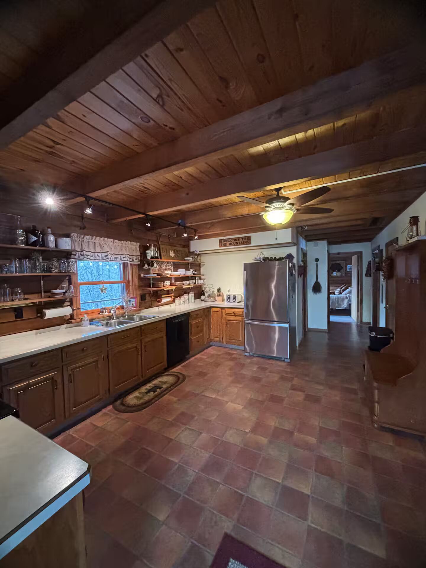 Eine rustikale Küche mit Holzschränken, einem Edelstahlkühlschrank und einem Schild mit der Aufschrift 'Welcome to the Mountains'.