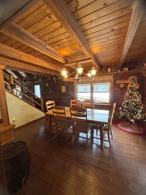 A wooden cabin interior with a dining table, chairs, a staircase, and a decorated Christmas tree. - Log Cabin - Hot Tub - Near Kalahari & Camelback (Newfoundland)