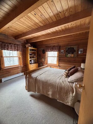 Een slaapkamer in een vakantiehuisje met een groot bed, een houten kast en twee ramen met gordijnen.