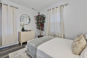 Ein Schlafzimmer mit einem Bett, einem Schminktisch, einem Spiegel, einer Zimmerpflanze und Vorhängen.
