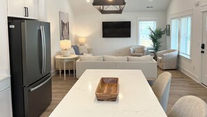 Et moderne køkken med marmor bordplade, et sort køleskab, en træbakke og et spiseområde med sofa og stole.