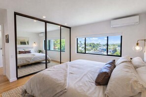 Ein Schlafzimmer mit einem großen Bett, Blick auf die Stadt und einer Schiebetür zu einem weiteren Raum.