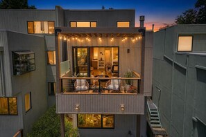 En moderne bygning med flere etager, en balkon, store vinduer og lyskæder.