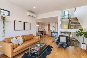Ein modernes Wohnzimmer mit Ledersofa, Glastisch und einer Treppe, die zu einer oberen Ebene führt.