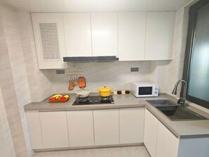 Een kleine keuken met witte kastjes, een magnetron, een spoelbak en een kookplaat met pannen.
