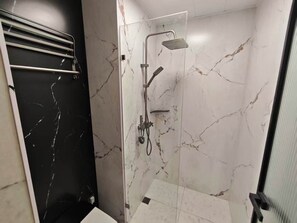 Een douche met een handdouche, een muurkranen en een glazen deur, met een wand betegeld in zwart.