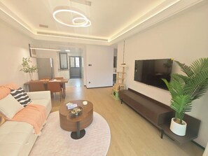 Een moderne woonkamer met een bank, salontafel, televisie en een plant.