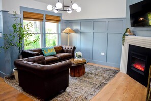 Ein Wohnzimmer mit einem braunen Ledersofa, einem Holztisch, einem Kamin und einem an der Wand befestigten Fernseher.