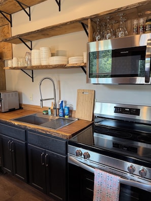 A kitchen with a stainless steel oven, a microwave, a sink, and wooden shelves above.