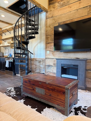A room with a spiral staircase, a fireplace, a television, and a wooden chest.