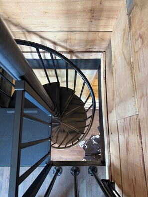 A spiral staircase with metal railings and wooden steps, leading to an upper floor.