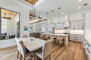 A modern kitchen with a central island, wooden flooring, and white cabinetry. - Luxury Coastal Beach Escape w/ Pool, Hot Tub & walkable to the beach (Marco Island)