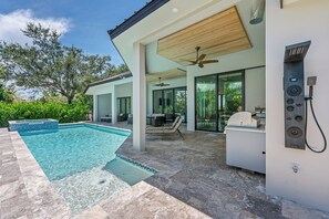 A modern outdoor pool area with a built-in hot tub, ceiling fans, and a stone-tiled patio. - Luxury Coastal Beach Escape w/ Pool, Hot Tub & walkable to the beach (Marco Island)