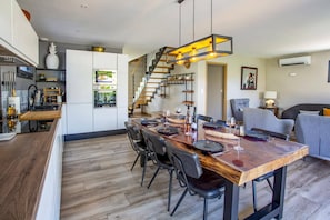 Eine moderne Küche mit einer Holztheke, ein Essbereich mit großem Tisch und eine Treppe, die in eine obere Ebene führt.
