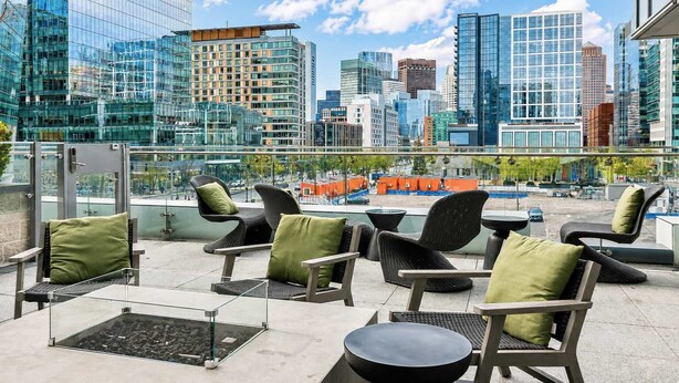 Terraza en la azotea con mobiliario exterior, vistas a un horizonte urbano y una barandilla de vidrio.