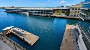 Un hotel frente al agua con muelle, un edificio grande con fachada de vidrio y un cielo azul despejado.