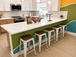 A modern kitchen with white cabinets, a built-in microwave, a stove, and a large island with bar stools. - Key and Code Stays: The Adventure House (St. Augustine)