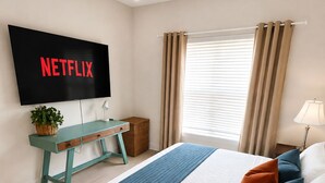 Een slaapkamer met een bed, een aan de muur bevestigde televisie, een bureau en een raam met gordijnen.