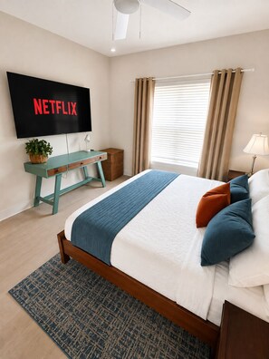 A bedroom with a bed, a TV mounted on the wall, a desk, and a window with curtains. - Key and Code Stays: The Adventure House (St. Augustine)