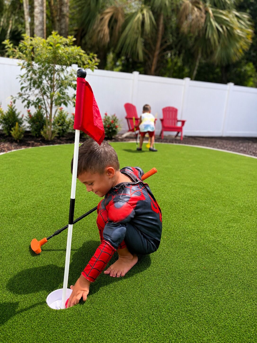 A child in a Spider-Man costume playing golf on artificial grass.
