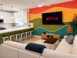 A modern living room with a sofa, a coffee table, and a TV mounted on the wall displaying 'NETFLIX'. - Key and Code Stays: The Adventure House (St. Augustine)