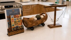 Een aanrecht met een houten mand met decoratieve eieren, een boek getiteld 'Key & Code Stays' en een hangweegschaal.