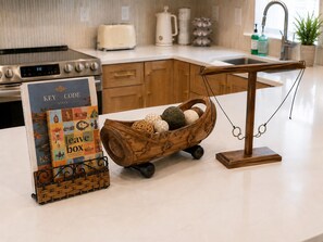 A kitchen counter with a wooden basket holding decorative eggs, a book titled 'Key & Code Stays,' and a hanging scale. - Key and Code Stays: The Adventure House (St. Augustine)