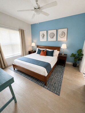 Ein Schlafzimmer mit einem Bett, Nachttischen, einem Deckenventilator und einem Fenster mit Vorhängen.