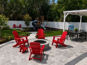 Eine Terrasse mit roten Adirondack-Stühlen, einer Feuerstelle und einer weißen Pergola.