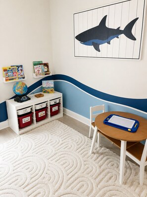 Ein Kinderzimmer mit Schreibtisch, Bücherregalen, einem Globus und einem Gemälde von einem Hai.