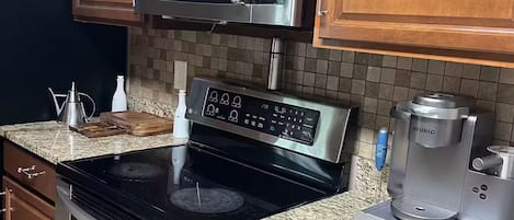 A kitchen with wooden cabinets, a stainless steel microwave, an oven, a coffee maker, and granite countertops.