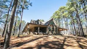 A large, two-story stone house surrounded by tall pine trees.
