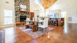 A spacious living area with a stone fireplace, wooden ceiling, and a large dining table.