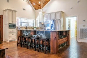 A kitchen with white cabinets, a stone island with stools, a stainless steel refrigerator, and a wooden ceiling. - The Perfect Oxford Basecamp for Families, Friends & Rebels (Water Valley)