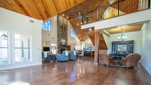 A spacious living area with a high ceiling, stone wall, and a balcony with a railing.