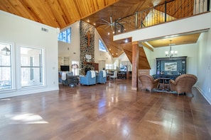 A spacious living area with a high ceiling, stone wall, and a balcony with a railing.